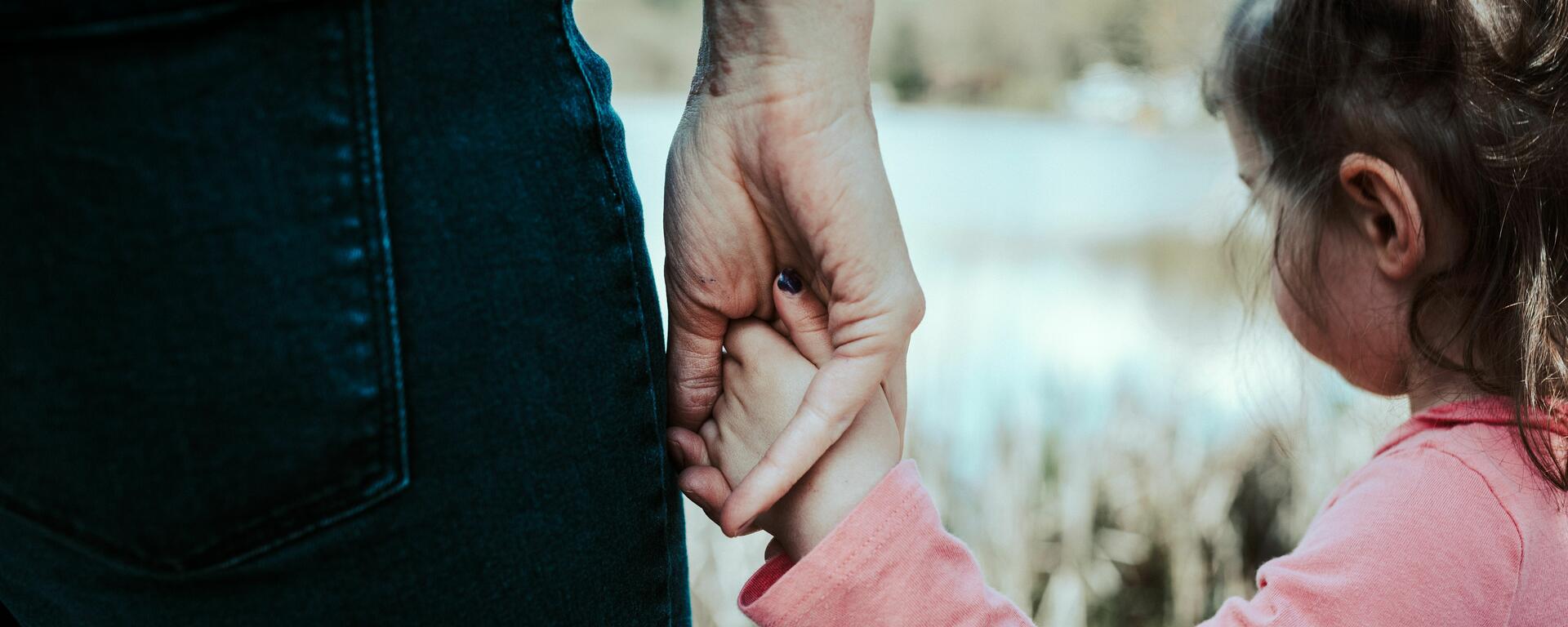 A child in a pink shirt holds the hand of their parent