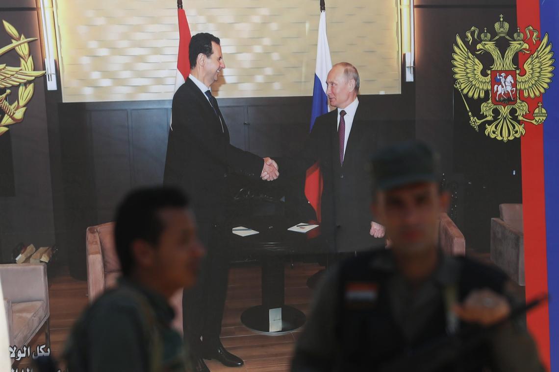 Syrian policemen stand guard in front of poster of Syrian President Bashar Assad and Russian President Vladimir Putin at a checkpoint on the entrance of the central Syrian town of Rastan in 2018.