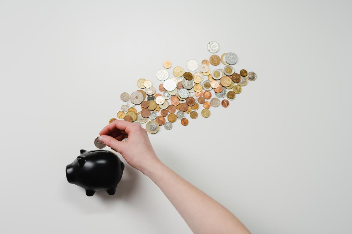 A hand places coins into a black piggy bank.