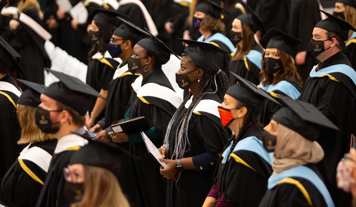 Graduates stand in their black caps and gowns, holding their degrees as they watch the stage during a convocation ceremony in 2021.. 