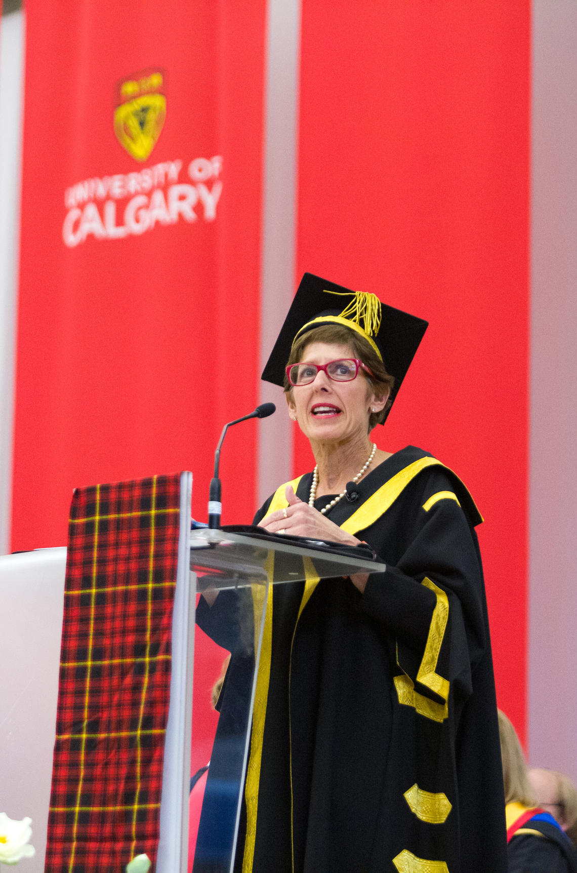 Chancellor Deborah Yedlin speaks at a podium in front of a red UCalgary banner during the convocation ceremony on 