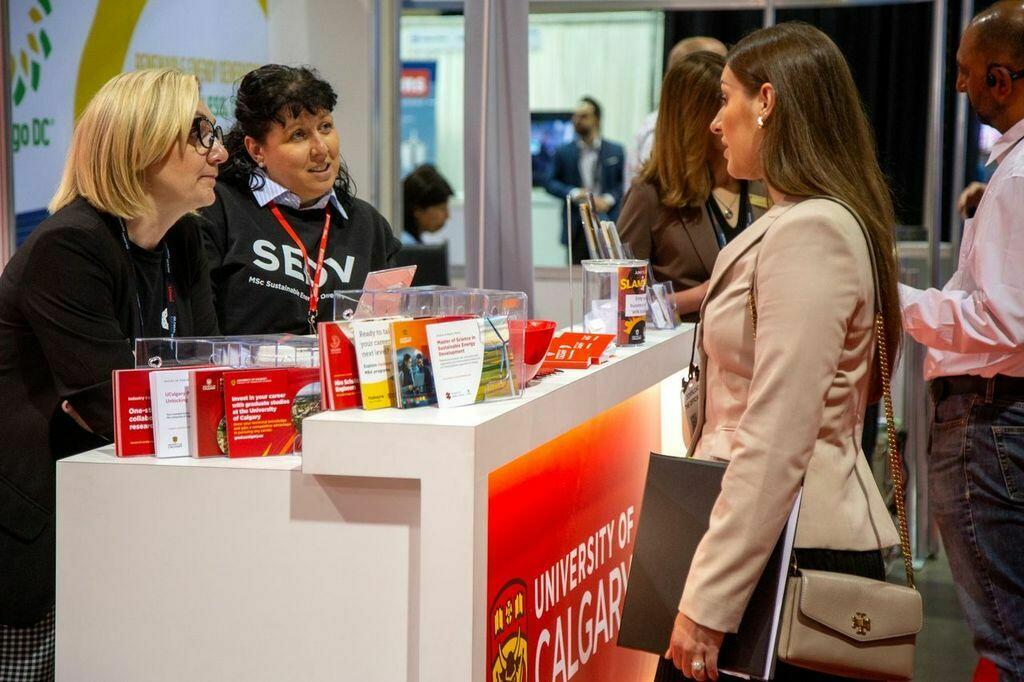 UCalgary Booth at the Global Energy Show. Two UCalgary representatives greet someone at the booth.