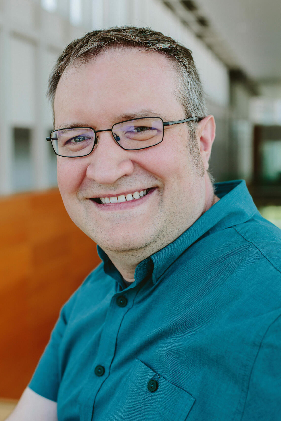 Tyson Kendon, a fair man with short hair and glasses, is wearing a button up shirt and smiling.