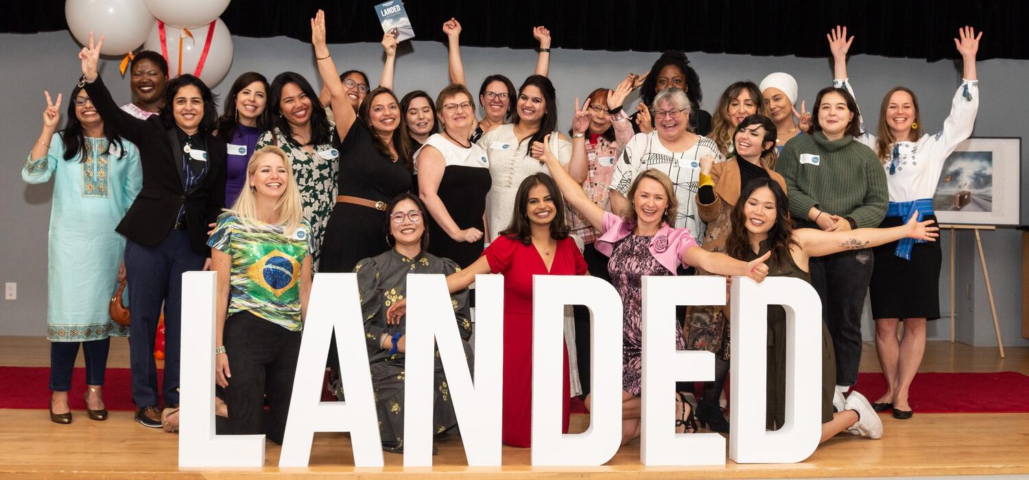 Co-authors of Landed: Transformative Stories of Canadian Immigrant Women celebrate book launch in front of Landed sign.