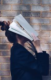 School Girl with Book in front of natural rustic red brick background holding book up to her face