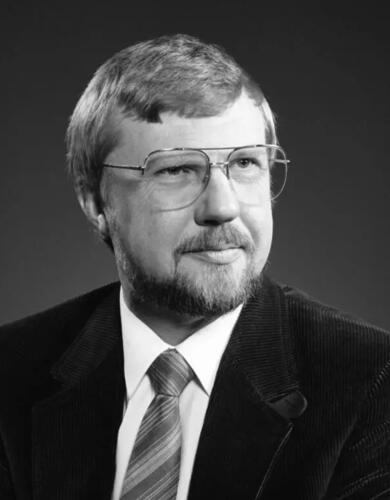 A black and white headshot of a man in a suit with glasses