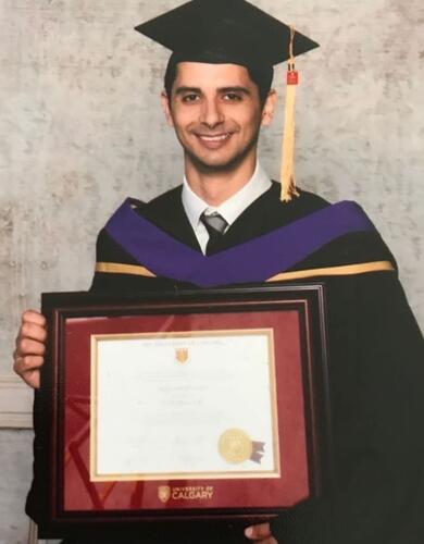 man in graduation gown and mortarboard, holding his framed degree