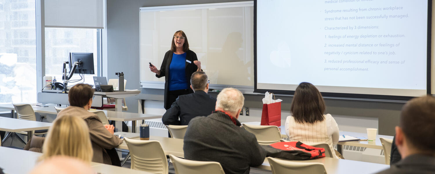 Lorelei stands at the front of a room speaking to an audience. On the screen a slide that says "what is burnout" is visible.