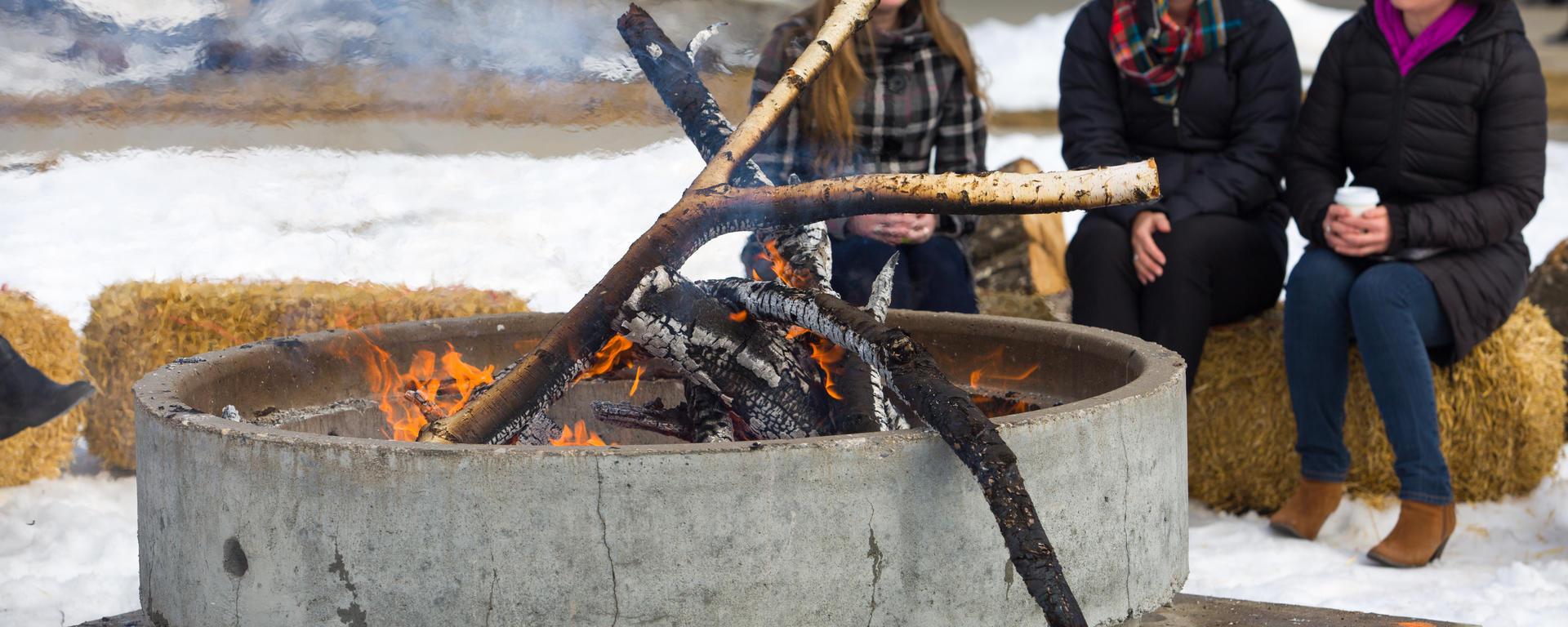 Three women sit around an outdoor firepit laughing
