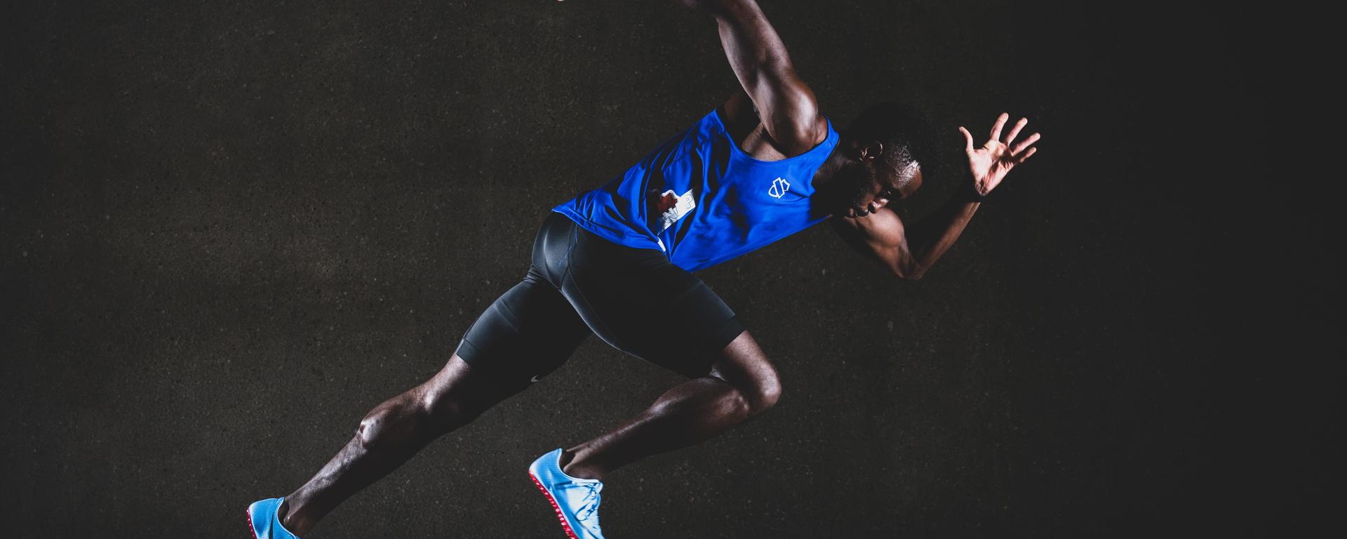 A man wearing a blue sports tank top, black shorts, moving in a sprinting motion