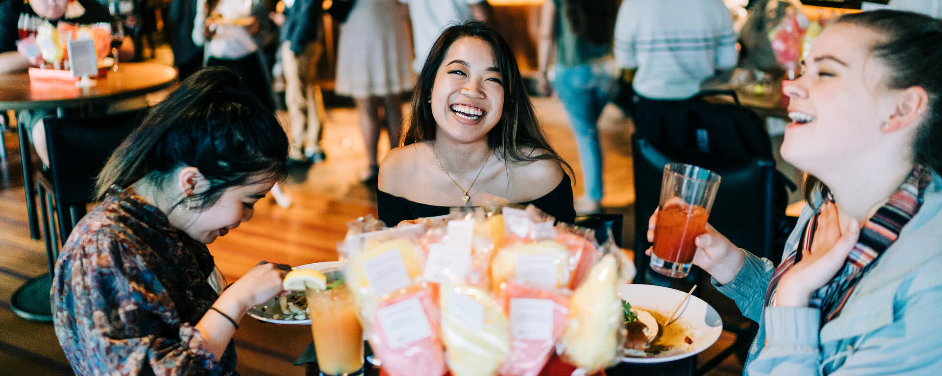 Three women laughing and talking at a table full of treats