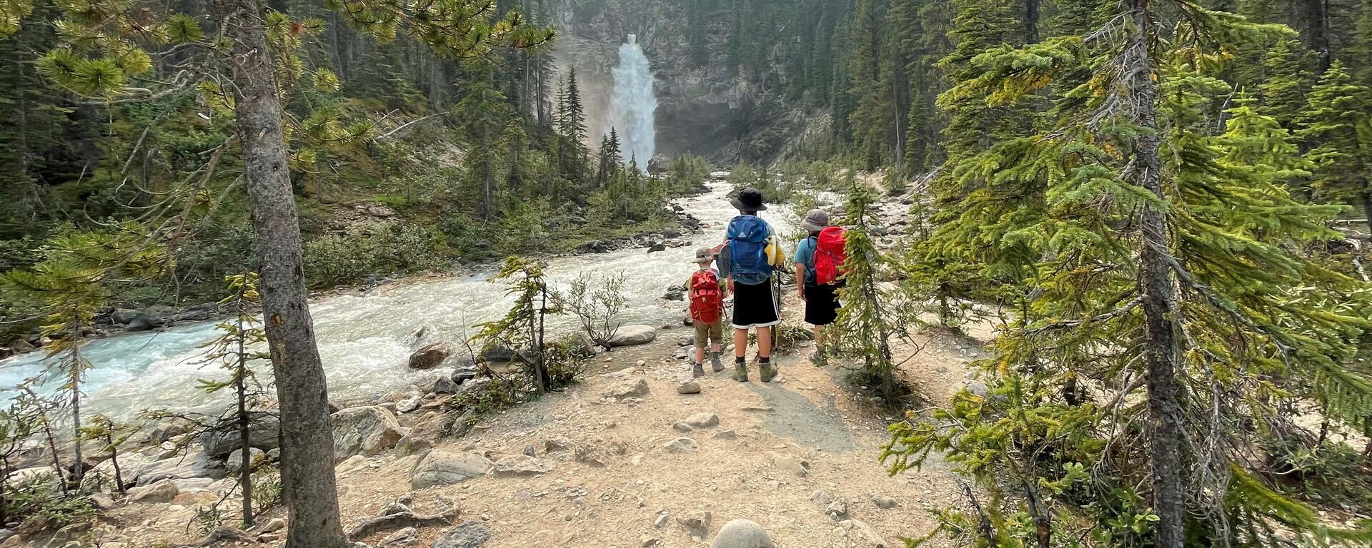 A photograph of three children standing beside a river with their backs to the camera