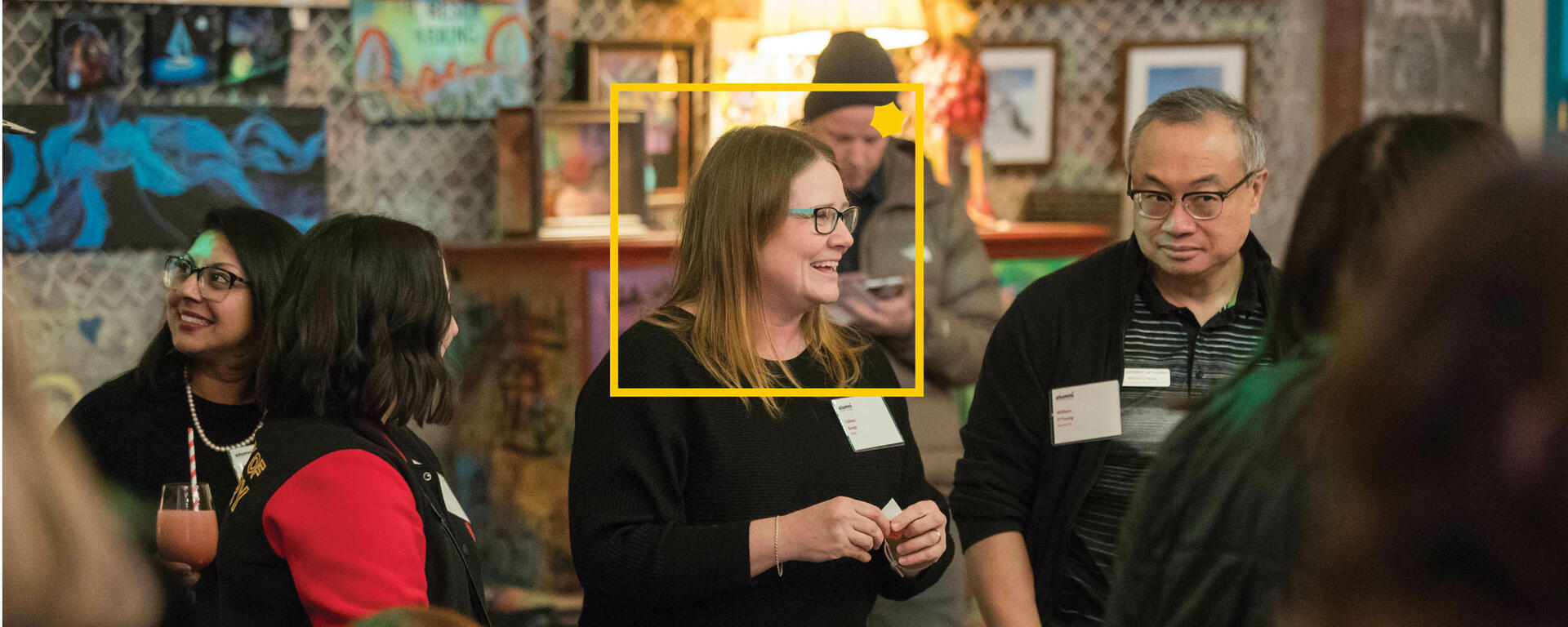 A photo of various board members laughing at an event with a yellow UCalgary alumni square and pop overlayed on the image.