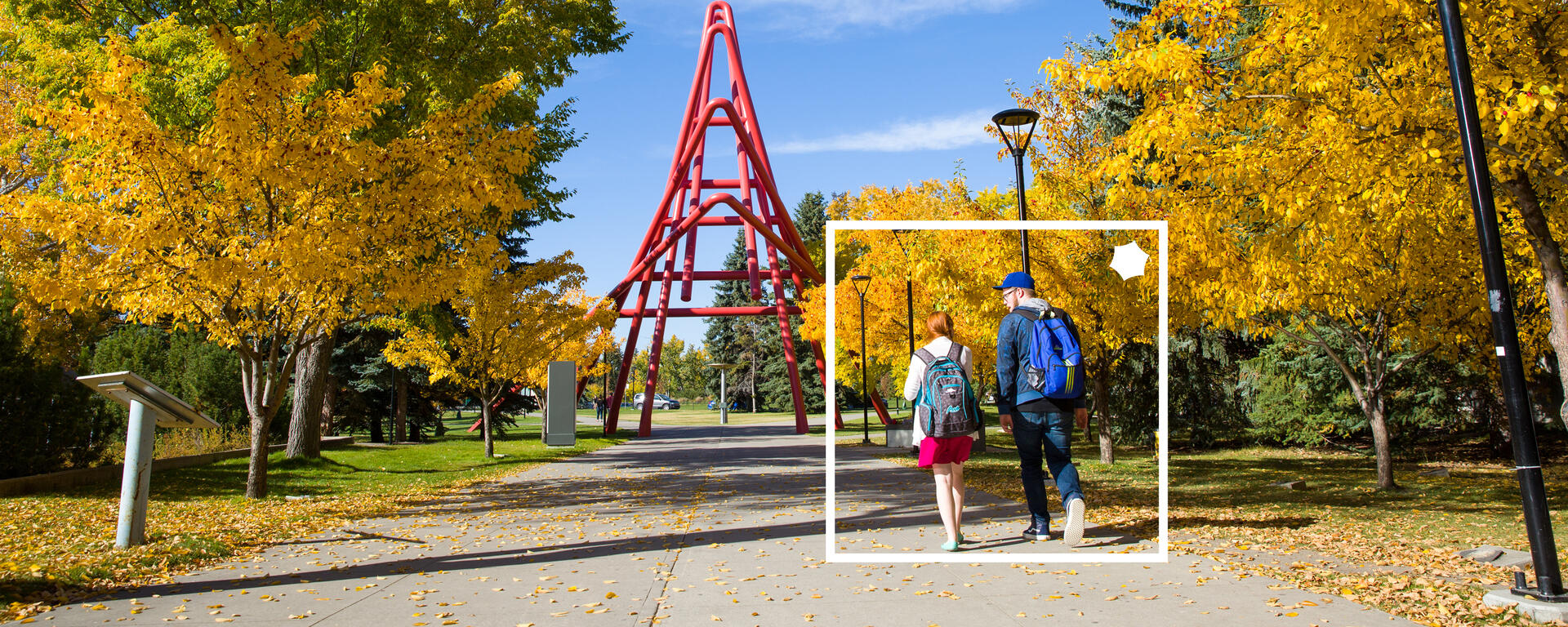 Two students walk under autumn trees toward the red sculpture on the University of Calgary campus.