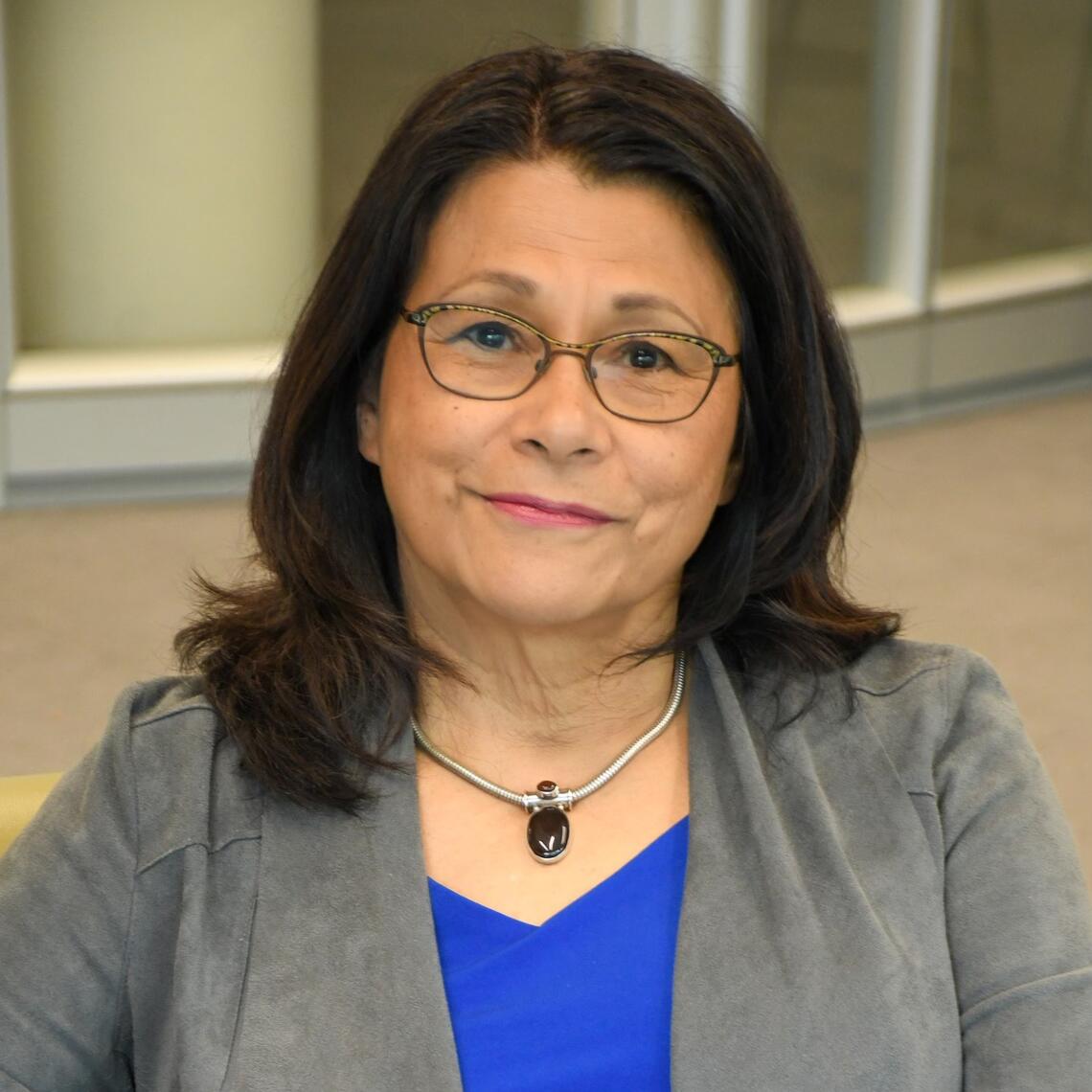 A photo of Dr. Verna St. Denis wearing a blue shirt and a grey blazer.