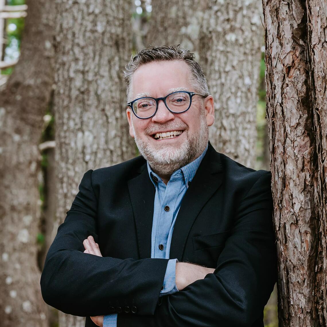 Smiling man leaning on tree.