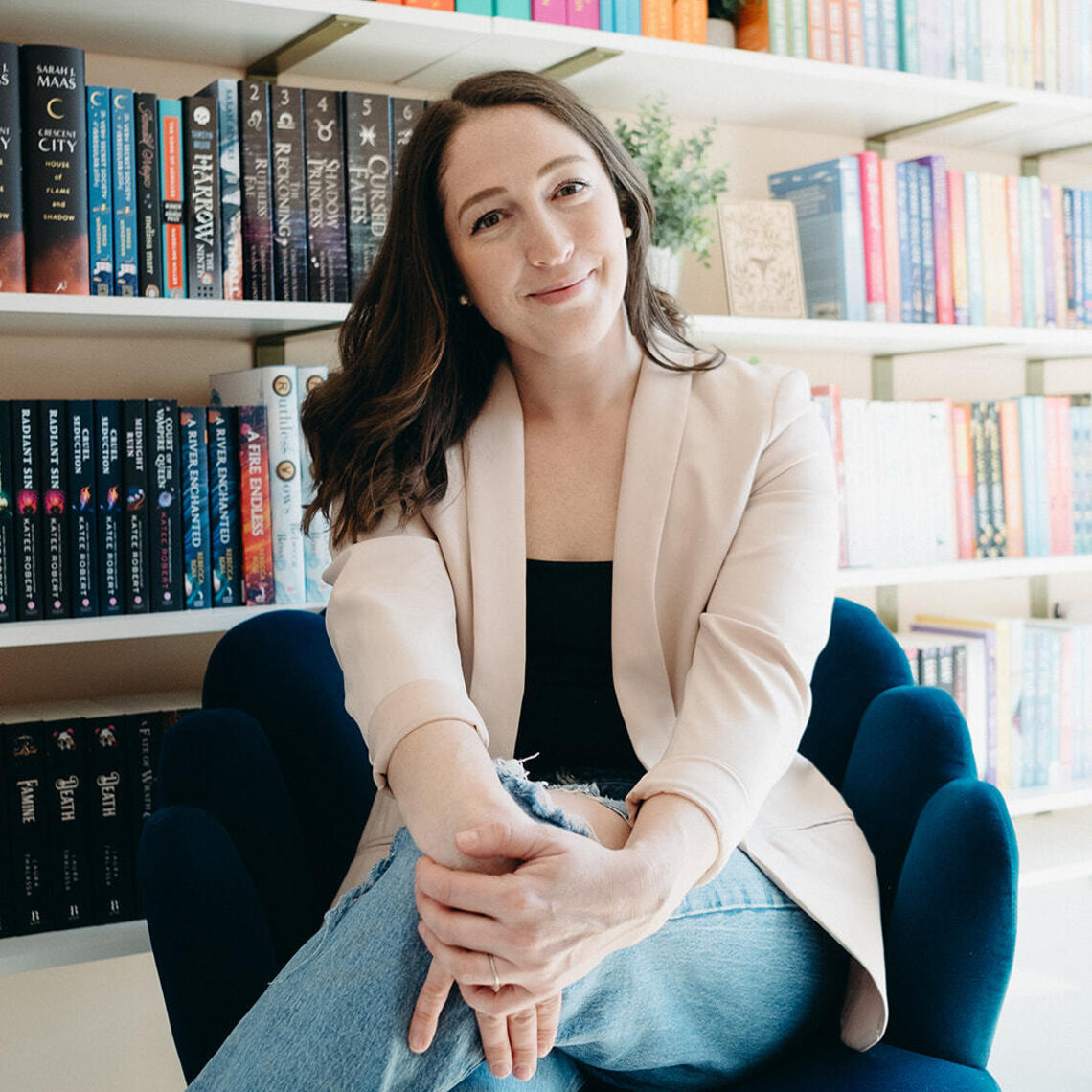 A photo of Shannon sitting in a chair in front of a book shelf, smiling.