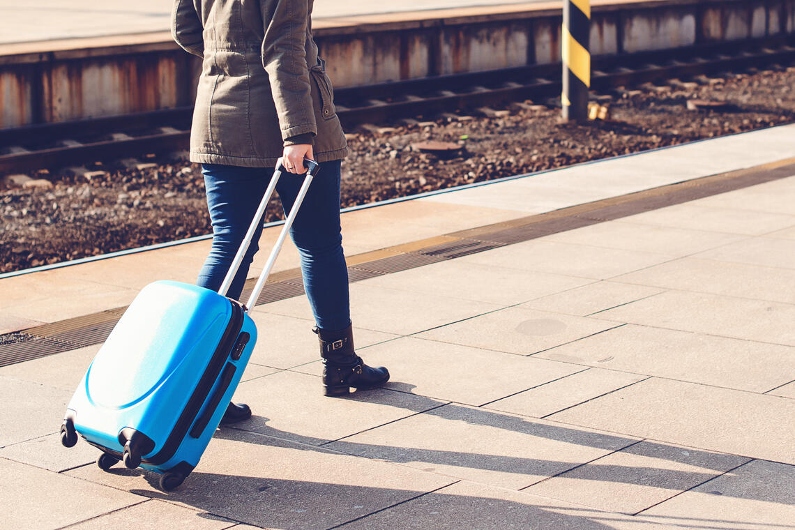 A person rolling a small carry-on luggage on a sidewalk