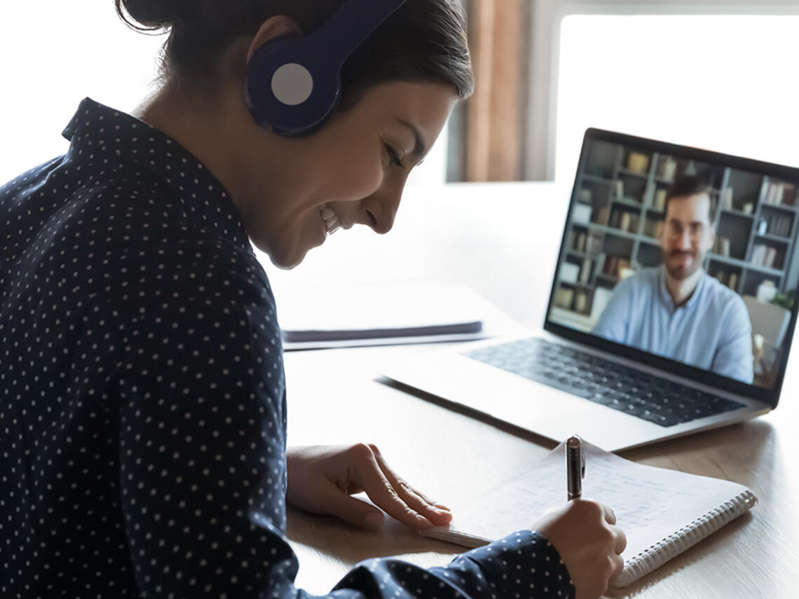 Person in an online meeting, taking notes on paper.