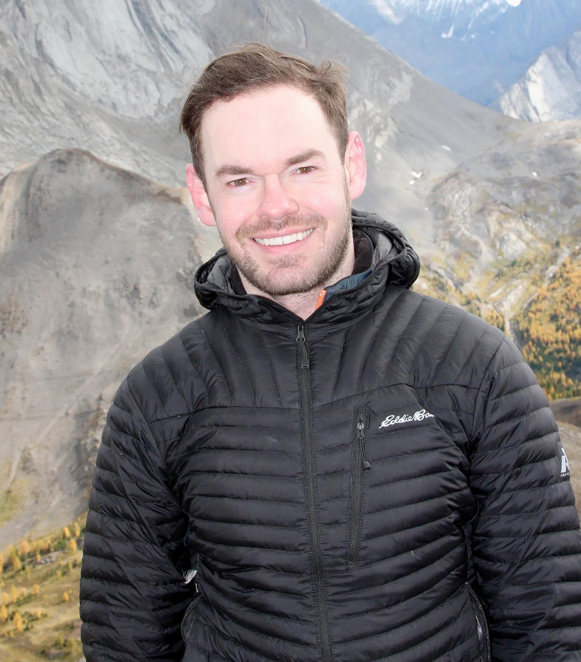Andrew Barry stands in front of a mountain in a black jacket