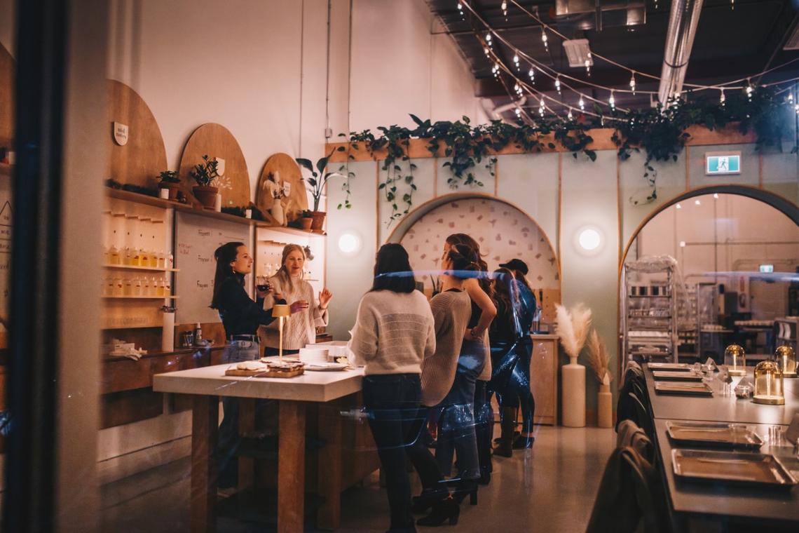 Women gathered around a table with drinks in their hand in the Milk Jar Candle Co. workshop