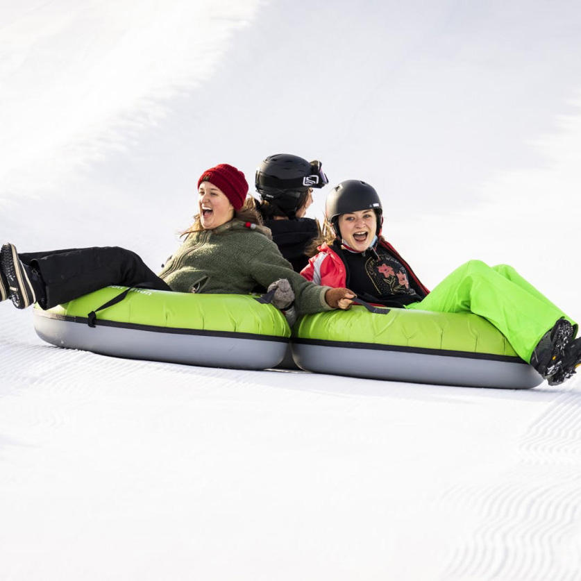 Three people riding down the snow in green tubes