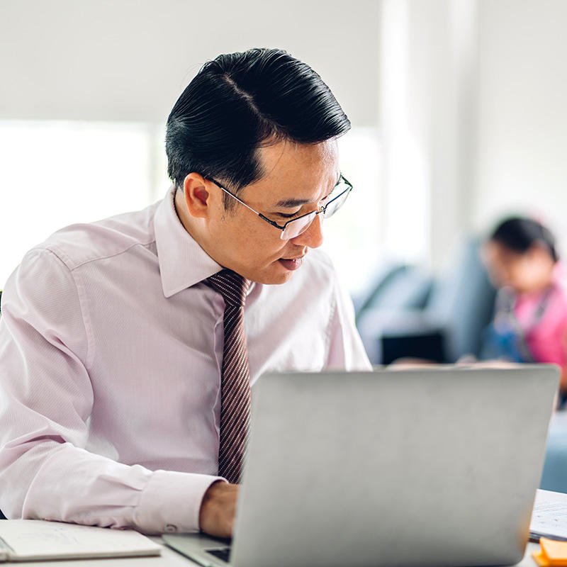 Image of a man sitting in front of a laptop and staring at papers beside his laptop