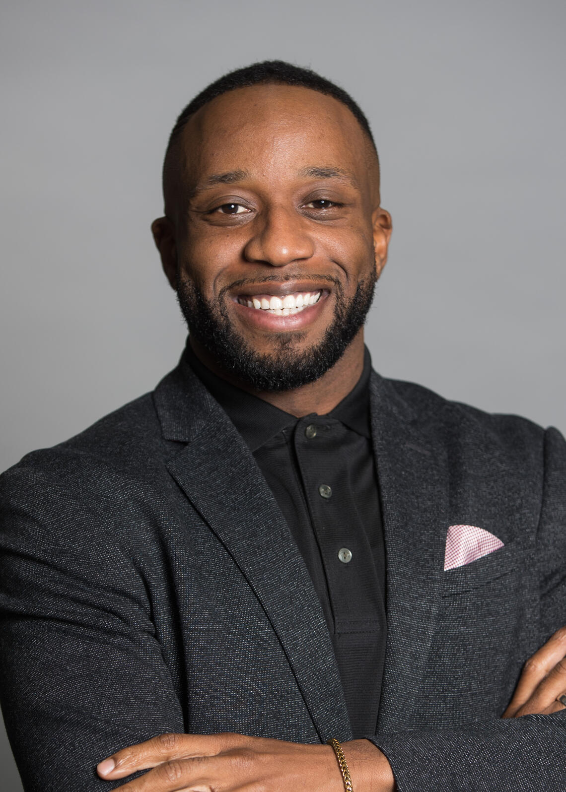 A photo of Angelo wearing a suit in front of a grey background