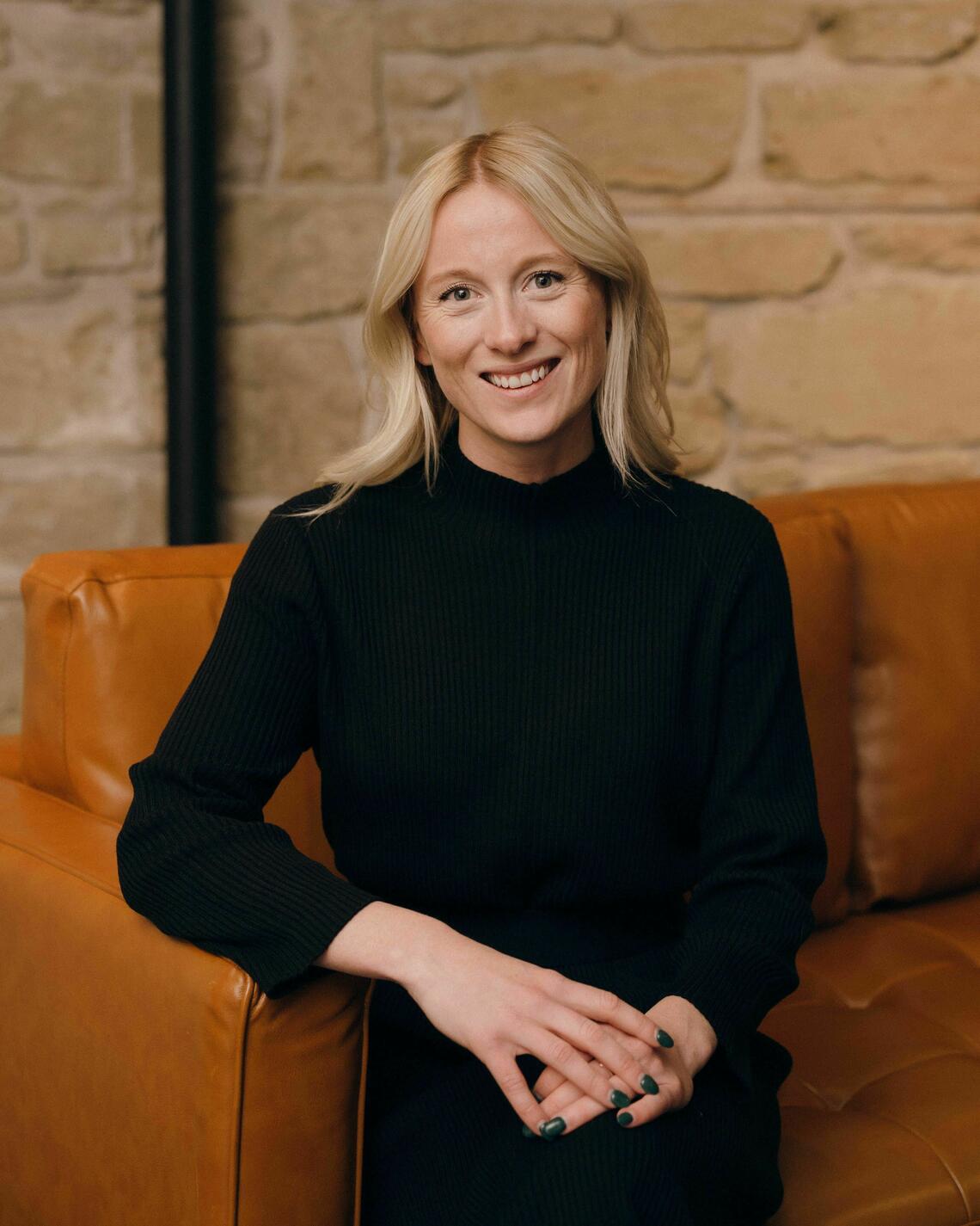 A photo of Danielle wearing a black blouse while sitting on an orange couch