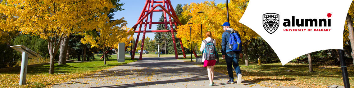 Two students walk under autumn trees toward the red sculpture on the University of Calgary campus.