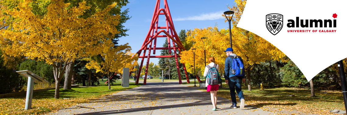 Two students walk under autumn trees toward the red sculpture on the University of Calgary campus.
