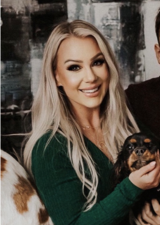 portrait of Jacquilynne Ellison-Wickson wearing a green v-neck sweater, holding a dog