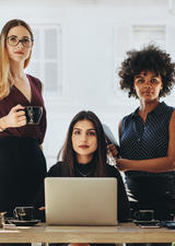 Four business women gathered around the table and staring into the camera